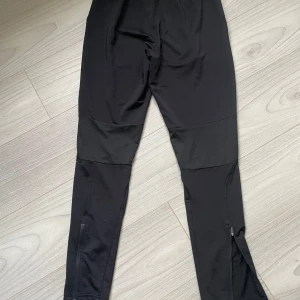 Svarta träningstights från Puma S - Svarta träningstights från Puma med DryCell-teknologi, smal passform och dragkedjor vid bensluten. Byxorna har meshpaneler för extra ventilation och en liten vit Puma-logga samt siffran 24 på låret. Perfekta för sport eller gym.