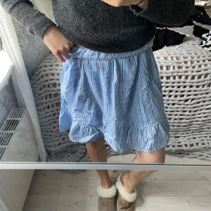 Blå randig kjol - Blå kjol med vita och mörkblå ränder. Omlottkjol med volang nertill och resår i midjan. Lätt och luftig i materialet och lite längre i modellen men går att vika ner. 