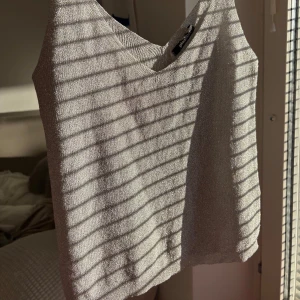 Glittrig silver linnetopp Gina Tricot - Säljer en snygg glittrig silverfärgad linnetopp från Gina Tricot. Toppen har smala axelband, v-ringning och är croppad i modellen. Perfekt för dig som vill sticka ut med lite extra shine. Materialet är stretchigt och följsamt.