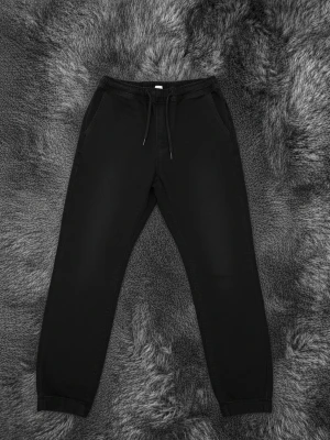 Svarta jeans med snörning - Säljer ett par svarta mjukisbyxor med resår i midjan och snörning framtill. Byxorna har två sidofickor och två bakfickor samt muddar vid bensluten för en skön passform. Perfekta för chill dagar eller när du vill vara bekväm.