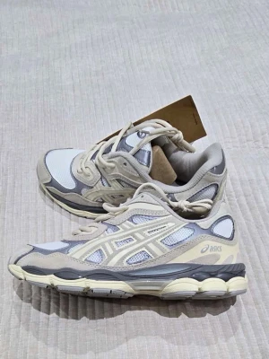ASICS sneakers  - Säljer ett par fräscha ASICS sneakers med snygga detaljer i beige, grått och vitt. Skorna har meshpaneler för bra ventilation, robust snörning och en chunky sula som ger skön komfort. Perfekt för dig som gillar stilrena och sportiga sneakers.