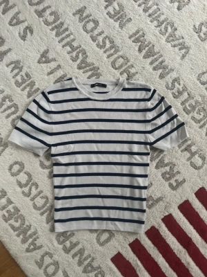 Vit och marinblå randig t-shirt Gina Tricot - Säljer en fräsch vit t-shirt med marinblå horisontella ränder från Gina Tricot. T-shirten har rund hals och korta ärmar, perfekt för en chill och stilren look. Materialet är mjukt och känns skönt mot huden.