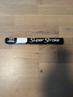 Svart Super Stroke tour 2.0 grepp - Säljer ett svart och vitt puttergrepp från Super Stroke med tydlig logga och stilren design. Greppet har en avlång form och är gjort för golfklubbor, perfekt för dig som vill ha bättre kontroll på greenen. Passar till dig som gillar snygga detaljer på golfutrustningen. Dessutom kommer de en grepp tejp med! 
