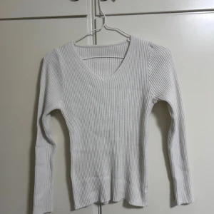 Vit ribbad långärmad tröja - Säljer en vit långärmad tröja med ribbad struktur och v-ringad hals. Tröjan har en slim passform och är gjord i ett mjukt stickat material som känns skönt mot huden. Perfekt att styla med jeans eller kjol för en clean look.