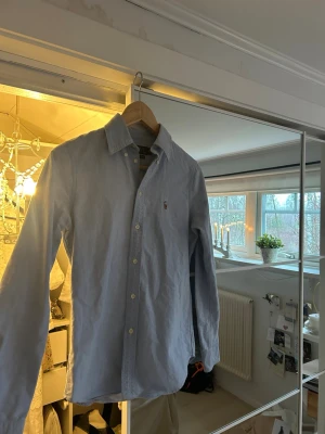 Ljusblå skjorta från Polo Ralph Lauren - Säljer en ljusblå skjorta från Polo Ralph Lauren i storlek XS. Skjortan har klassisk krage och knappar hela vägen.