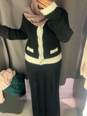 Svart och vit kofta med pärlknappar - Snygg svart kofta med vita ribbade detaljer och pärlknappar framtill. Koftan har två dekorativa fickor med pärldetaljer och rund halsringning. Perfekt för dig som gillar klassisk stil med en twist. Långärmad och mjukt stickad material.