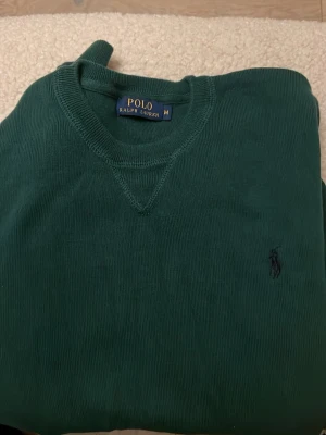Grön tröja från Polo Ralph Lauren - Snygg grön tröja från Polo Ralph Lauren i storlek M. Tröjan har rund hals och diskret broderad logga på bröstet. Tillverkad i mjuk bomull som känns skön mot huden. Perfekt för dig som gillar klassisk stil med en modern touch.