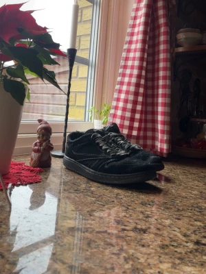Travis scott nike Jordan 1 low  - Säljer ett par svarta Nike Air Jordan 1 Lows med vit kontrastsöm och svart-vita snören. Skorna har en klassisk rund tå, perforerad tåbox och är tillverkade i mocka och skinn. Air Jordan-loggan syns tydligt på hälen. Perfekta för dig som gillar streetwear.
