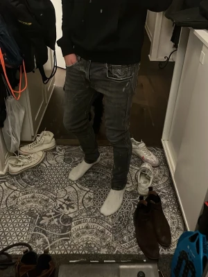 Slitna Replay jeans mörkgrå  - Säljer ett par Replay jeans i svart tvättad färg med coola slitningar och kontrastsömmar. Modellen har klassiska fem fickor, dragkedja och knapp, samt Replay-logga på fickan. Jeansen har en slim passform och raka ben, tillverkade i stretchig bomull för skön känsla.