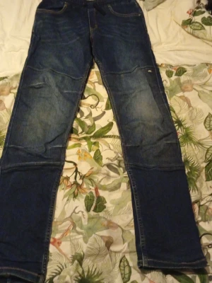 Jeansbyxor från Ossoami - Säljer ett par mörkblå jeansbyxor från Ossoami i storlek 170. Byxorna har klassisk femficksdesign, broderade detaljer på bakfickorna och förstärkta sömmar vid knäna. Materialet är slitstarkt jeans och passformen är rak med normal midja. Pris kan sänkas vid en villig affär.