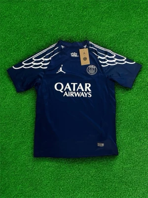 PSG fotbollströja  - Bilderna visar en mörkblå PSG fotbollströja med vita detaljer och Qatar Airways-logga, men inga skor finns med.