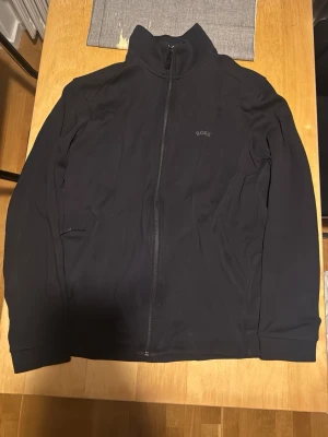 Svart zip-kofta från BOSS, storlek M - Svart kofta från BOSS med hel dragkedja och diskret logga på bröstet. Modellen har hög krage och långa ärmar