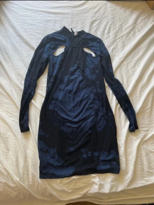 Mörkblå cut-out klänning - Snygg mörkblå kortklänning med unika cut-out detaljer vid axlarna och långärmad design.  Klänningen har ett batik liknande mönster och är gjord i mjuk bomull som känns skön mot huden.  Perfekt för dig som gillar att sticka ut med coola detaljer och trendig look. Tyvärr har klänningen 3 små hål på magen (se bilderna). Storlek L. Från H&M. 