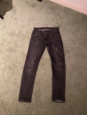 Replay jeans med slitningar - Säljer ett par svarta jeans från Replay, modell med fem fickor och klassisk jeanslook. Jeansen har en mörk tvätt med lätt slitna detaljer och sitter slim längst benen. Perfekt för dig som gillar en klassisk look.