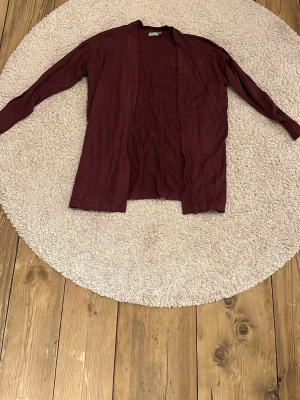 Vinröd kofta från Fransa, storlek L - Säljer en vinröd, långärmad kofta från Fransa i storlek L. Koftan har öppen front utan knappar och är gjord i ett mjukt, tunt material som känns skönt mot huden. Perfekt att slänga över en t-shirt eller linne när det blir lite kyligt.