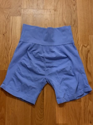 Blå högmidjade träningstights shorts - Säljer ett par blå träningstights shorts med hög midja och ribbade detaljer längs sidorna. 