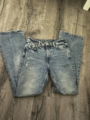 Blå utsvängda jeans med slitningar - Säljer ett par blå utsvängda jeans med klassisk femficksdesign och snygga slitningar på ena låret. med en cool tvättad look. Perfekta för en avslappnad och trendig stil. Pris kan diskuteras💋