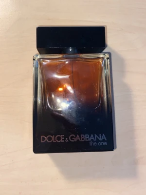 Dolce & Gabbana The One edp parfym - Snygg parfymflaska från Dolce & Gabbana, modellen The One. Flaskan är fyrkantig med svart lock och har en gradient från mörkbrun till svart. Glasmaterialet ger en lyxig känsla och designen är stilren och modern. Perfekt för dig som gillar exklusiva dofter. 90-95%full flaska 100ml.
