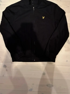 Svart vindjacka från Lyle & Scott - Snygg svart vindjacka från Lyle & Scott med gul broderad logga på bröstet. Den är i väldigt bra skick men den har regn fläckar på båda axlar👍