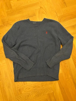 Mörkblå stickad tröja från Polo Ralph Lauren - Mörkblå stickad tröja från Polo Ralph Lauren med klassisk röd logga broderad på bröstet. Tröjan har rund halsringning, långa ärmar och ribbade muddar vid ärmslut och nederkant. Perfekt för lager på lager och enkel att matcha. Tröjan är storlek M fast passar bra som XS/S.