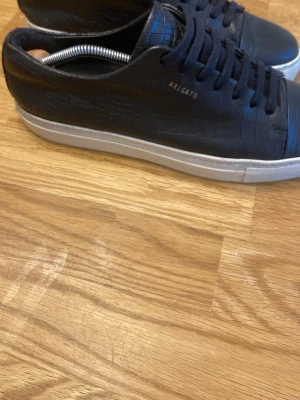 Svarta  Axel Arigatos - Stilrena svarta sneakers från Axel Arigato med croc-mönstrad ovandel i skinn och vit platt sula. Nästan helt oanvända. storlek 43. Har tyvärr inte lådan