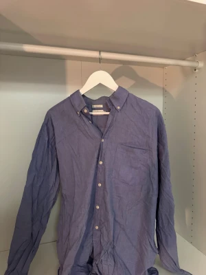 Blå skjorta från Uptown Classic - Säljer en blå skjorta från Uptown Classic i 100% bomull. Skjortan har klassisk krage med knappar, bröstficka och långa ärmar. Perfekt för dig som gillar en enkel och stilren look.