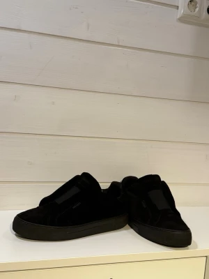 Svarta mockasneakers från Axel Arigato - Stilrena svarta sneakers från Axel arigato, mjuk mocka med diskret logga på sidan. Skorna har en klassisk låg siluett. Perfekta för dig som gillar minimalistisk design och exklusiva material.