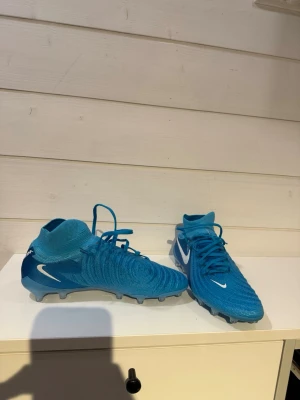 Nike blå fotbollsskor Phantom - Säljer ett par blå Nike Phantom fotbollsskor med vitt nikemärke. Använda en halv träning. Säljer då jag har breda fötter och bara använder tiempo.