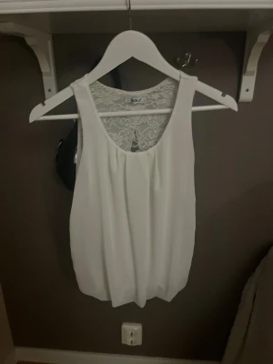 Vit ärmlös linnetopp med spetsdetalj - Säljer en vit ärmlös linnetopp med rund halsringning och snygg spetsdetalj i ryggen. Toppen har en luftig passform och ett öppet parti i ryggen. 