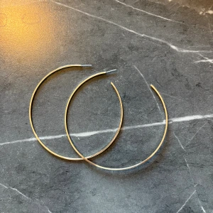 Stora tunna guldfärgade hoops - Säljer ett par stora, tunna örhängen i klassisk hoop-modell. De är guldfärgade och har en minimalistisk, rund form som ger en stilren look. Perfekta för dig som gillar enkel men trendig design.
