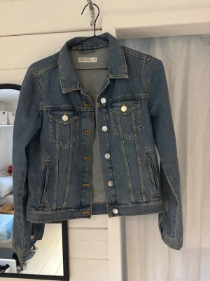 Blå klassisk jeansjacka cubus - Snygg blå jeansjacka från cubus med klassisk passform. Jackan har silverfärgade knappar framtill och på bröstfickorna, samt långa ärmar. 