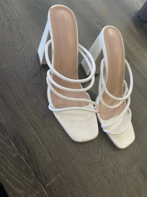 Vita pumps med remmar från Cincoro - Stilrena vita pumps från Cincoro med fyrkantig tå och flera tunna remmar över foten. Skorna har hög klack och öppen design som ger en trendig look. Perfekta för dig som vill sticka ut med en modern och chic stil. Endast använda en gång, plast kvar under sko. 