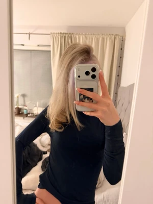 Svart långärmad  - Säljer en svart långärmad  i stretchigt material. Toppen har en tight passform och enkel, stilren design utan synliga detaljer. Perfekt att styla med jeans eller kjol för en clean look.