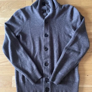 Brun kofta från Suitsupply - Säljer en stilren brun kofta från Suitsupply. Den har långa ärmar och knappar framtill. Perfekt för kyligare dagar med sin mjuka och bekväma passform. Ribbstickade detaljer vid krage, ärmslut och nederkant. Storlek S men sitter mkt bättre runt XS! Du får helst vara under 180cm för bästa möjliga passform. Mvh Oscar 