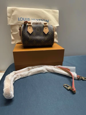  Monogram Mini Handväska - Säljer en brun minihandväska  med klassiskt monogrammönster och beige detaljer. Väskan har två korta handtag och avtagbar axelrem i läder. Kommer med dustbag och box. Perfekt accessoar för dig som gillar lyxig och tidlös design.