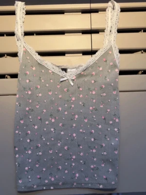 Sött linne med spets och blommor - Gulligt linne ifrån Divided som e grönt med rosa små blommor. Den har spets dekoration och en liten rosett.