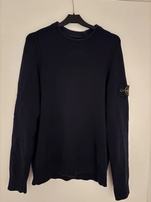 Mörkblå stickad tröja Stone Island - Säljer en mörkblå stickad tröja från Stone Island i storlek S. Tröjan har rund hals, ribbade muddar och den klassiska Stone Island-loggan på ärmen. Perfekt för dig som gillar stilrena och exklusiva plagg. Köpt på NK, Stone Island påse ingår.