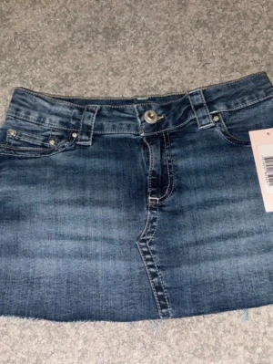 Blå jeanskjol med broderade fickor (xs) - Snygg blå jeanskjol i kort modell och broderade fickor från Nelly. Nyskick med prislapp.