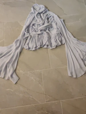 Ljusblå volangblus med långa ärmar - Supersöt ljusblå blus med volanger och långa, vida ärmar. Blusen har en romantisk känsla med flera lager och knytning framtill. Perfekt för dig som gillar en bohemisk och trendig stil. Materialet känns lätt och flowy. Nästan aldrig använd och i storlek M. har haft den en gång och den passar mig som har storlek S men armarna är väldigt långa. Fint skick i övrigt 