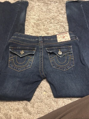 True Religion blå jeans  - Säljer ett par klassiska blå jeans från True Religion med ikoniska kontrastsömmar och stora fickor. Strl 25, slitage längst ner .