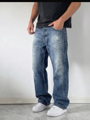 Blå diesel loose fit jeans - Säljer ett par blåjeans med loose fit och slitna detaljer. Jeansen har klassisk femficksdesign, normal midja och raka ben. Tillverkade i tålig bomullsdenim med en snygg tvättad look. Perfekta för en avslappnad och trendig stil.