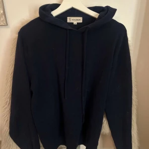 Mörkblå hoodie från Studios - Säljer en stilren mörkblå hoodie från Studios i storlek M. Tröjan är cashmere och slutsåld överallt! Nypris 1000, ett litet hål har den som går säkret o sy men annars fin.