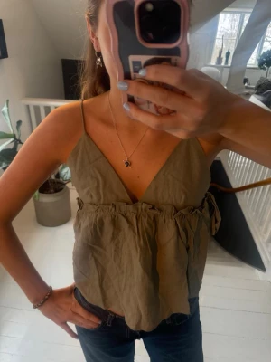 Grönt linne från Zara med rosettdetaljer – storlek M - Säljer ett grönt linne från Zara i storlek M med fina rosettdetaljer vid sidorna. Ett feminint och trendigt linne som passar perfekt till både vardag och festligare tillfällen. Lätt att styla med jeans, kjol eller kostymbyxor för en chic look.  Linnet är i mycket fint skick.