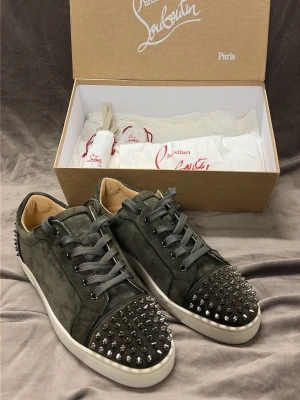 Mörkgröna Christian Louboutin sneakers - Säljer ett par mörkgröna sneakers från Christian Louboutin i mocka med coola silverfärgade nitar på tå och häl. Skorna har snörning, vit platt sula och en riktigt edgy vibe. Perfekta för dig som vill sticka ut med exklusiva detaljer och lyxig känsla.