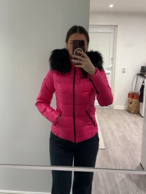 Rosa dunjacka med svart fuskpäls - Snygg rosa dunjacka från Rockandblue med svart päls runt kragen. Använd vid ett tillfälle. Köpt för 1700, säljer för 1199