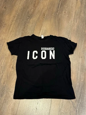 Svart Dsquared2 ICON t-shirt - Svart t-shirt från Dsquared2 med stor vit 'ICON'-text på bröstet. Klassisk rund hals och korta ärmar. Perfekt för dig som gillar streetwear och vill sticka ut med en tydlig logga. Tillverkad i mjuk bomull för skön känsla.