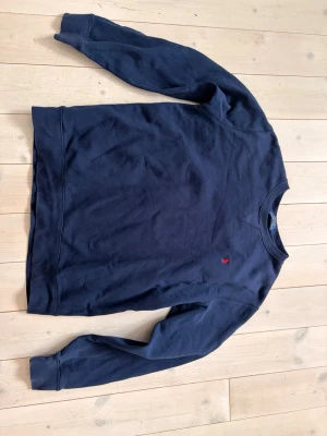Mörkblå sweatshirt från Polo Ralph Lauren - Klassisk mörkblå sweatshirt från Polo Ralph Lauren med rund halsringning och diskret röd logobrodyr på bröstet. Tröjan har ribbade muddar vid ärmslut och nederkant. Perfekt för en avslappnad och stilren look.