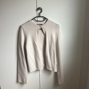 Beige kofta från Gina Tricot - Säljer en stilren beige kofta från Gina Tricot i storlek S. Koftan har lång ärm, rund halsringning och stängs med en knapp upptill. Mjuk och stickad känsla, perfekt för lager-på-lager under höst och vinter. 