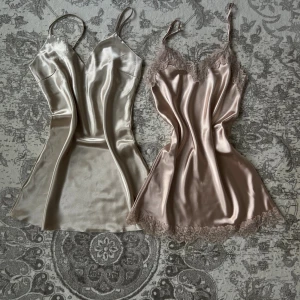 Två satinklänningar med smala axelband - Säljer två korta satinklänningar med smala axelband. Ena klänningen är champagnefärgad och enkel och den andra är ljusrosa med spetsdetaljer vid halsringning och fåll. 