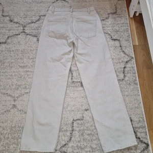 Ljusgrå raka jeans från Zara - Säljer ett par ljusgrå/vita jeans från Zara med raka ben och klassisk femficksdesign. Jeansen har bälteshällor och stängs med knapp och dragkedja. Perfekta för en clean och stilren look. Fint nu till höstsäsongen!